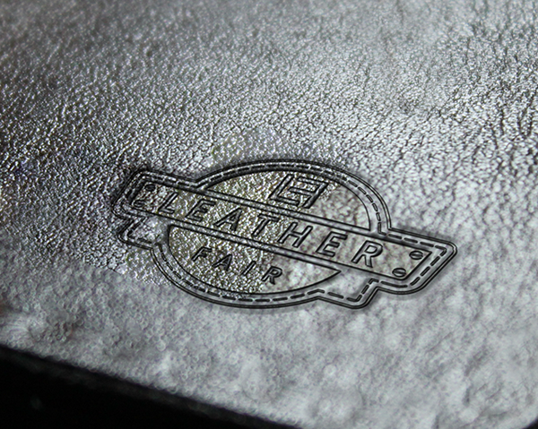 Close-up of a "LEATHER FAIR" logo embossed on metallic leather.